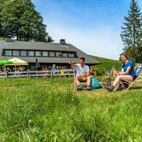 Ein Paar sitzend vor dem Almgasthaus Kn�pflesbrunnen. Beide genie�en den Ausblick sowie ein Getr�nk. 